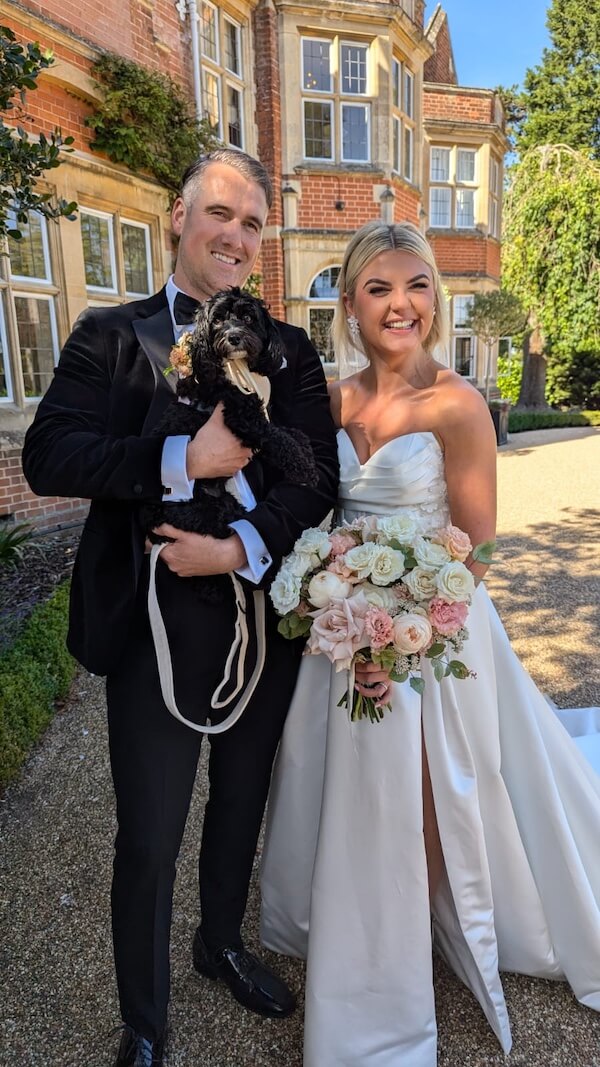 Wedding couple holding their dog whilst grinning
