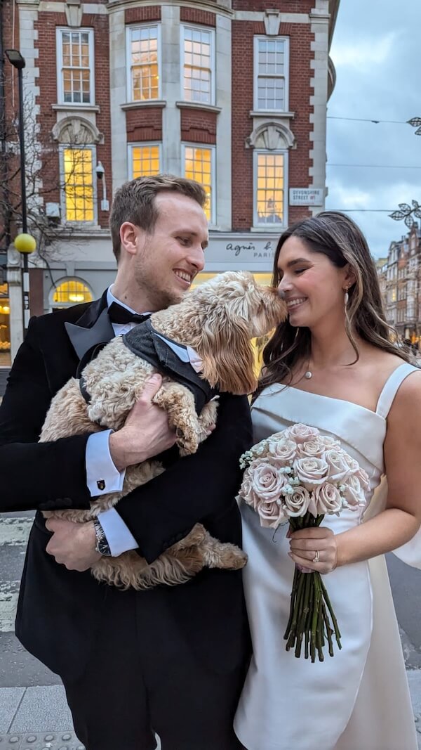 Wedding couple holding their dog whilst dog attempts to lick the bride's face