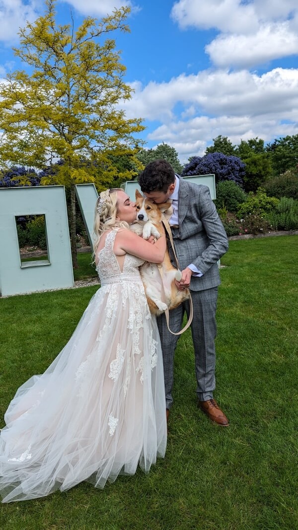 Wedding couple posing whilst kissing their dog on the head