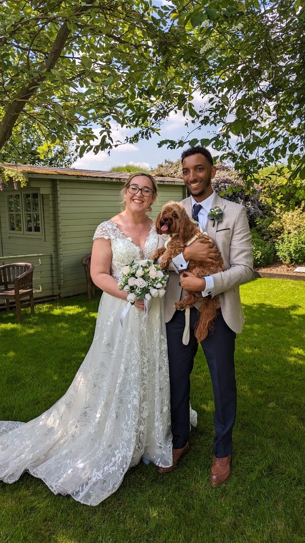Wedding couple standing under a tree holding their dog